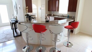 A modern kitchen with a central island, bar stools, and wooden cabinets. - Crystal Cove 1014 (Kissimmee)