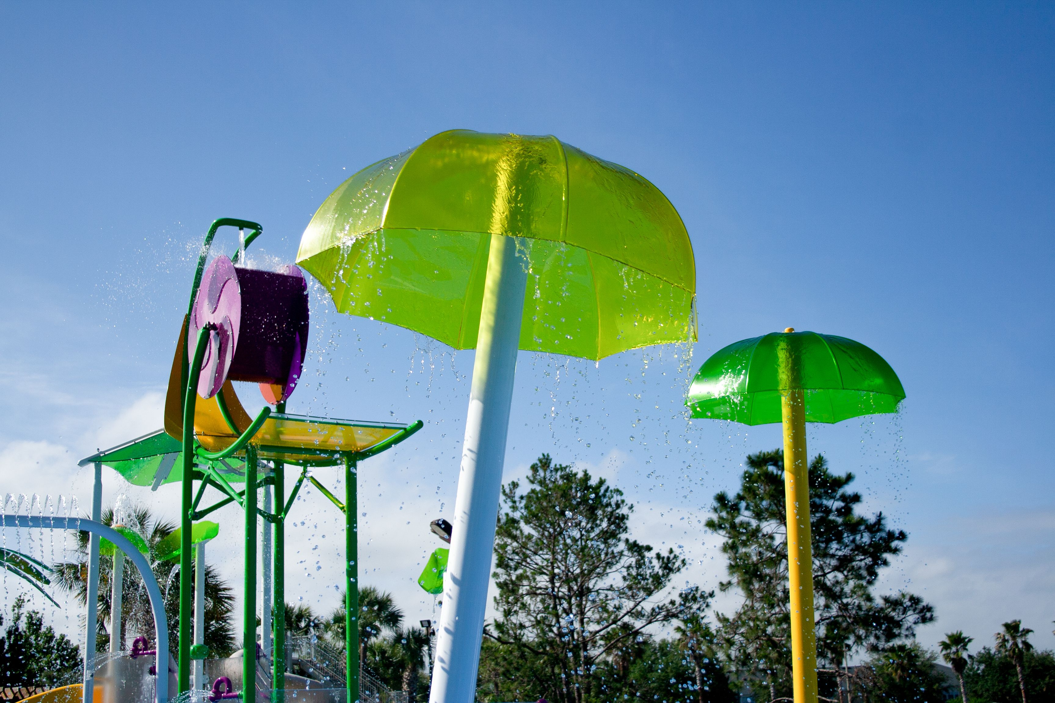 A water park with various water features including a large green umbrella and a water slide.