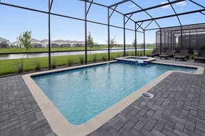 Une piscine entourée d’un patio, avec un espace salon couvert et une vue sur un quartier résidentiel.