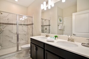 Une salle de bain moderne avec une douche à l’italienne, deux lavabos et un grand miroir.