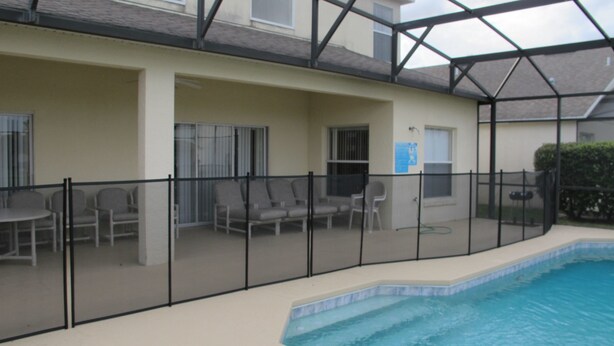 Une piscine intérieure dotée d’un toit en verre, entourée d’une clôture noire et aménagée avec plusieurs chaises et une table.
