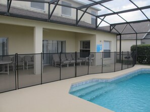 An indoor swimming pool with a glass ceiling, surrounded by a black fence, and furnished with several chairs and a table. - Cumbrian Lakes 4645 (Kissimmee)