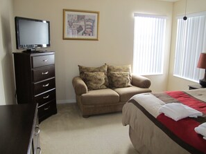A bedroom with a bed, a sofa, a dresser, a television, and a window with blinds. - Cumbrian Lakes 4645 (Kissimmee)