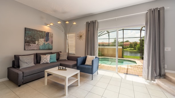 A modern living room with a sectional sofa, a coffee table, and a view of a swimming pool through large glass doors. - Encantada Resort 3143 (Kissimmee)