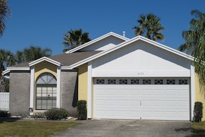 A single-story house with a garage, a small front yard, and palm trees in the background. - Indian Wells 3173 (Kissimmee)