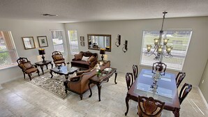 A spacious living room with a dining area, featuring a large wooden dining table, multiple chairs, a sofa set, and a chandelier. - Bella Vida 210 (Kissimmee)