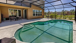 A covered outdoor swimming pool area with a patio, chairs, and a view of the neighborhood. - Bella Vida 210 (Kissimmee)