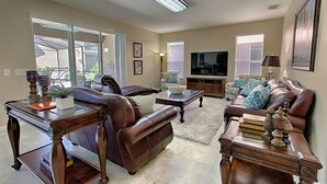 A living room with a brown leather sofa, a glass coffee table, a wooden side table, and a television. - Bella Vida 210 (Kissimmee)