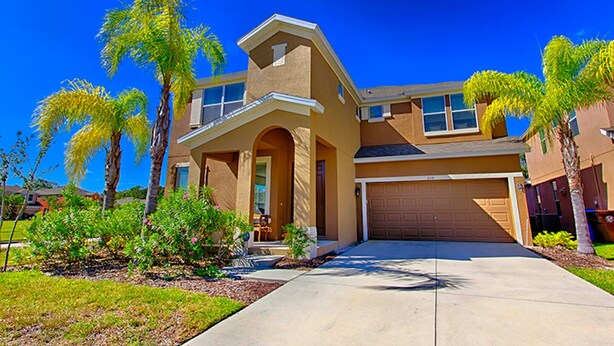 A two-story house with a front porch, garage, and palm trees. - Bella Vida 210 (Kissimmee)