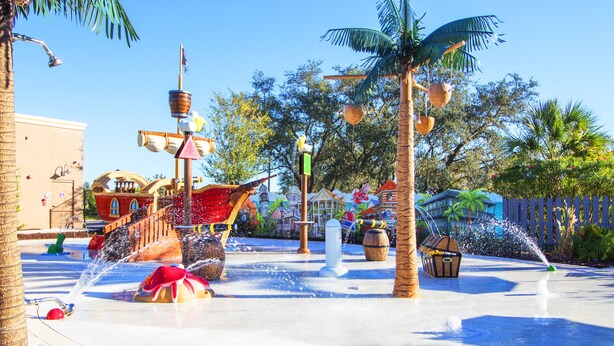 A water fountain with a pirate ship theme, palm trees, and a building in the background. - Festival Resort 313 (Davenport)