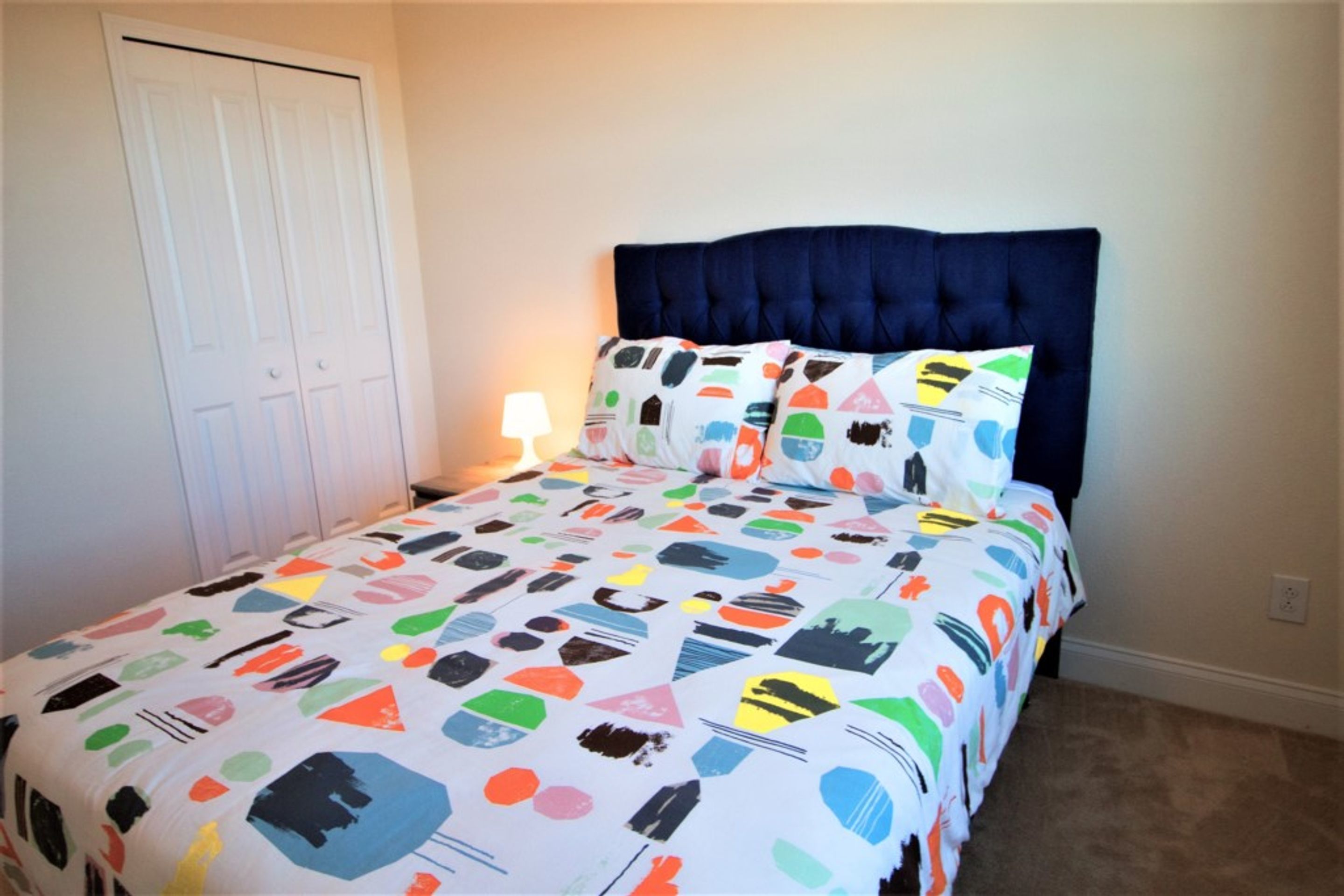 A bedroom with a bed, a nightstand, a lamp, and a door.