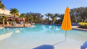 A clear swimming pool with lounge chairs and umbrellas, surrounded by palm trees and a building with outdoor seating. - Festival Resort 313 (Davenport)
