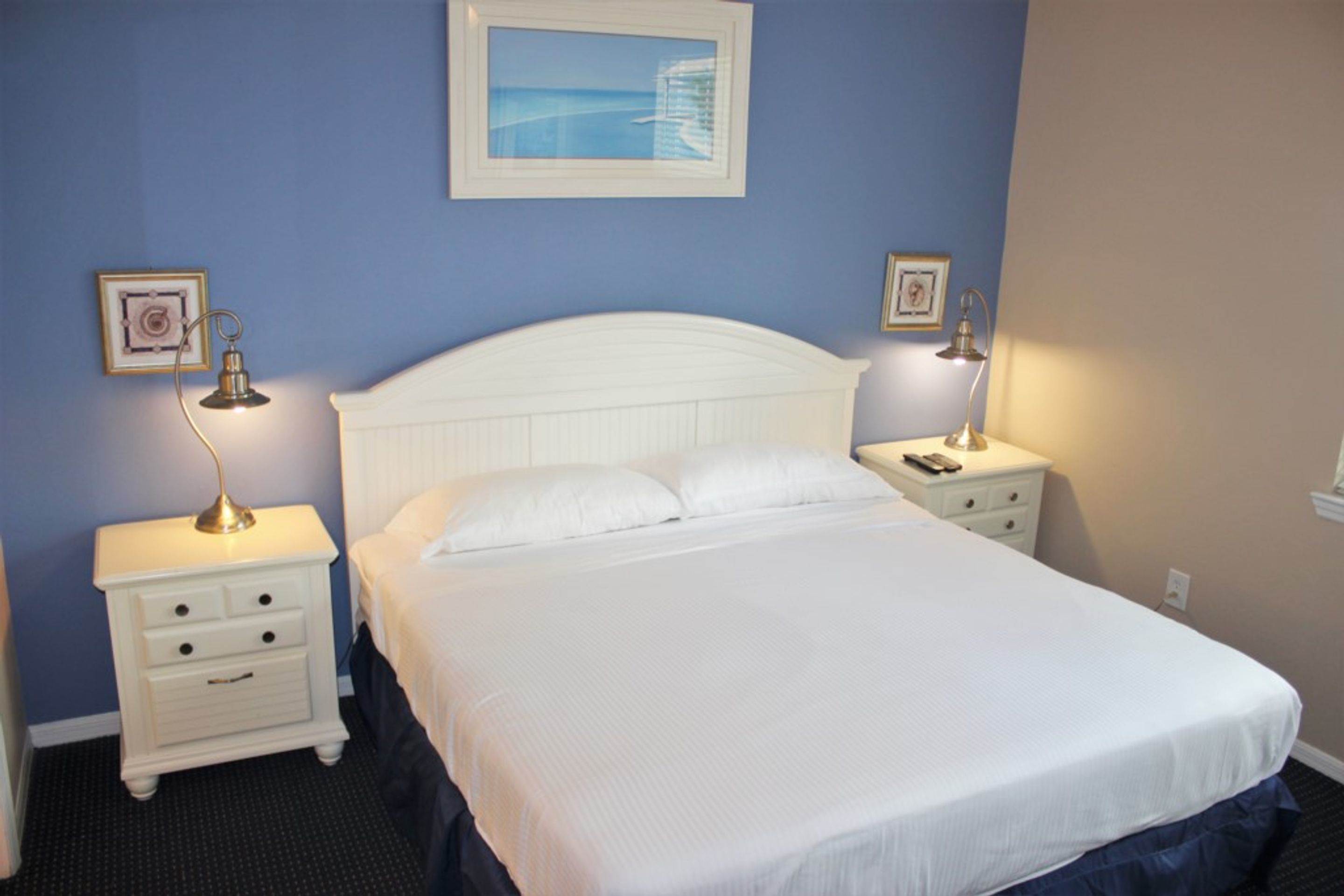A neatly made bed with white linens, two bedside tables with lamps, and framed pictures on the walls.