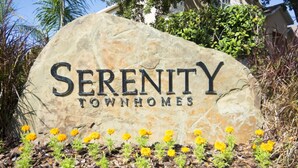 A stone sign with "Serenity Townhomes" written on it, surrounded by yellow flowers and mulch. - Serenity 17428 (Clermont)