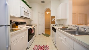 A modern kitchen with white cabinetry, a microwave, stove, and double sink. - Windsor Palms Condos 8102 - 305 (Kissimmee)