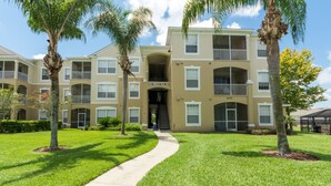 A multi-story apartment building with a central entrance, balconies, and a well-maintained lawn. - Windsor Palms Condos 8102 - 305 (Kissimmee)