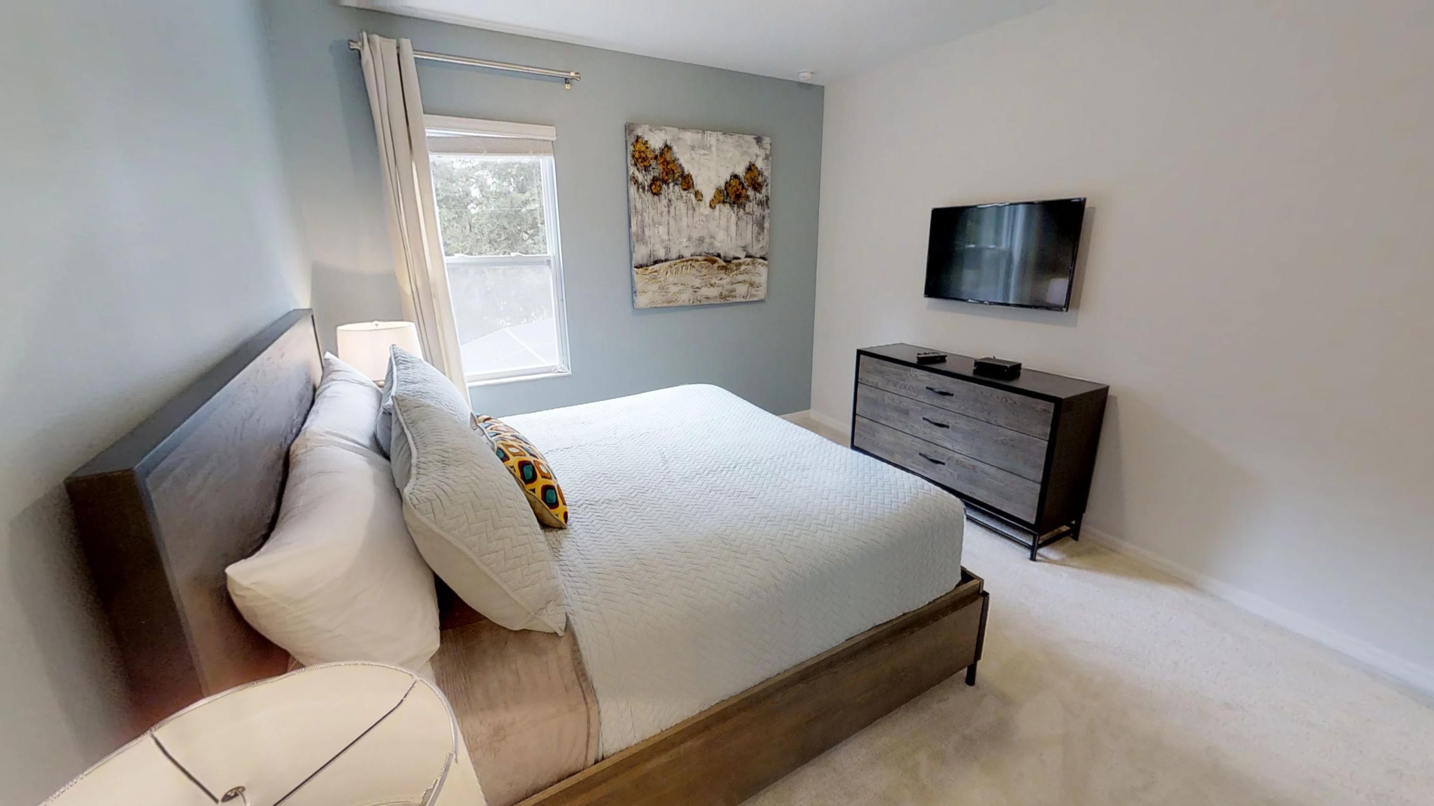 Une chambre à coucher avec un lit, une commode, un téléviseur et des œuvres d’art accrochées au mur.