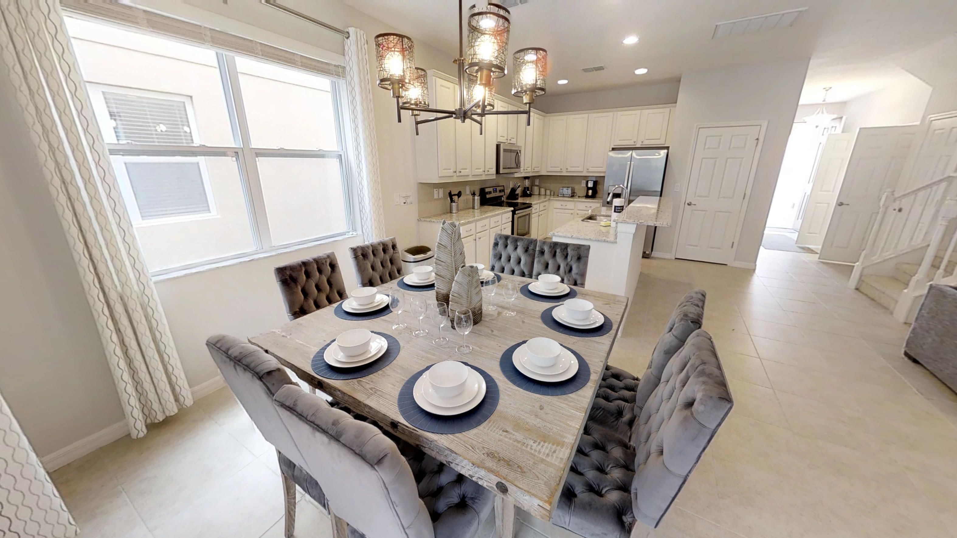 A dining area with a wooden table set for six, surrounded by upholstered chairs.