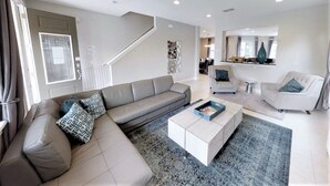 Un salon moderne avec un canapé d’angle gris, une table basse blanche et un tapis à motifs.