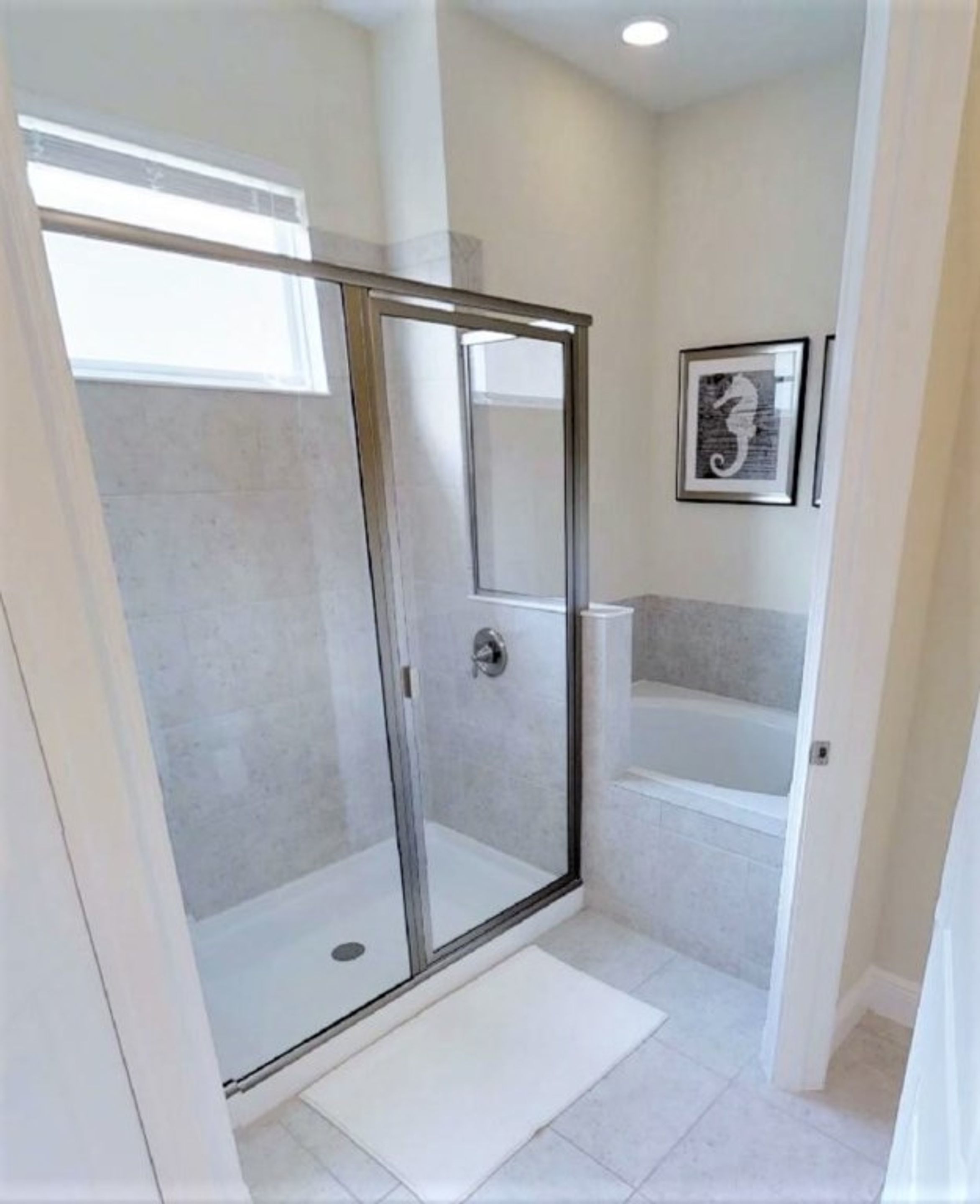 A modern bathroom with a glass shower enclosure, a bathtub, and a framed seahorse artwork on the wall.