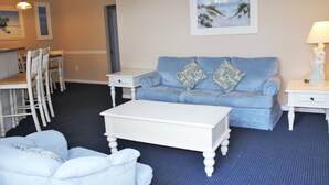 Een zithoek met een blauwe bank, witte fauteuils, een witte salontafel en een schilderij aan de muur.