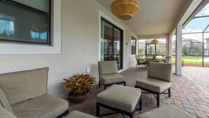 A covered patio area with cushioned seating, a table, and a potted plant. - Champions Gate 1470 (Davenport)
