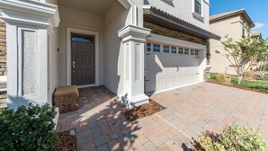 A two-story house with a front entrance, a garage, and a landscaped driveway. - Champions Gate 1470 (Davenport)