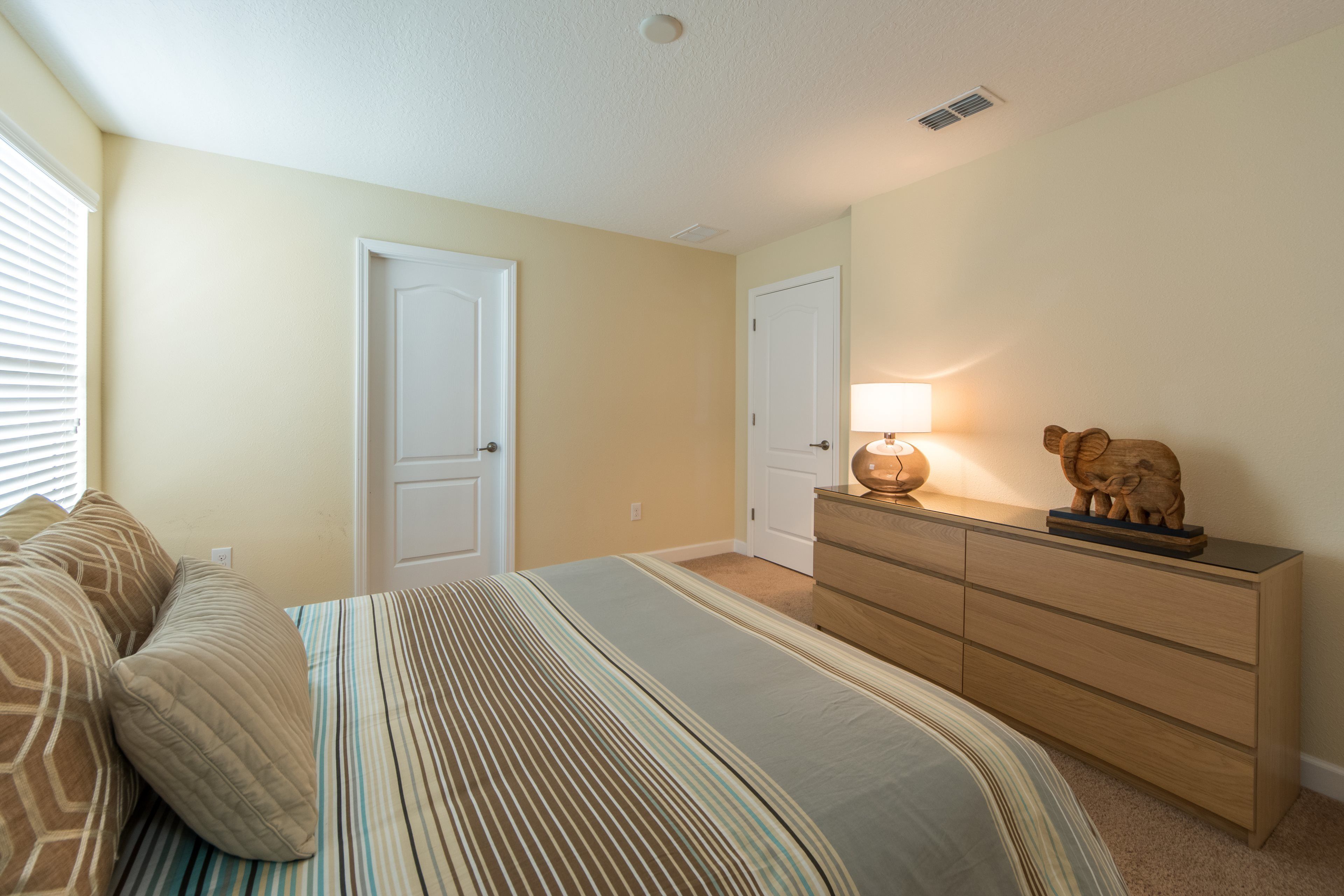 A bedroom with a bed, two doors, a dresser, and a lamp.