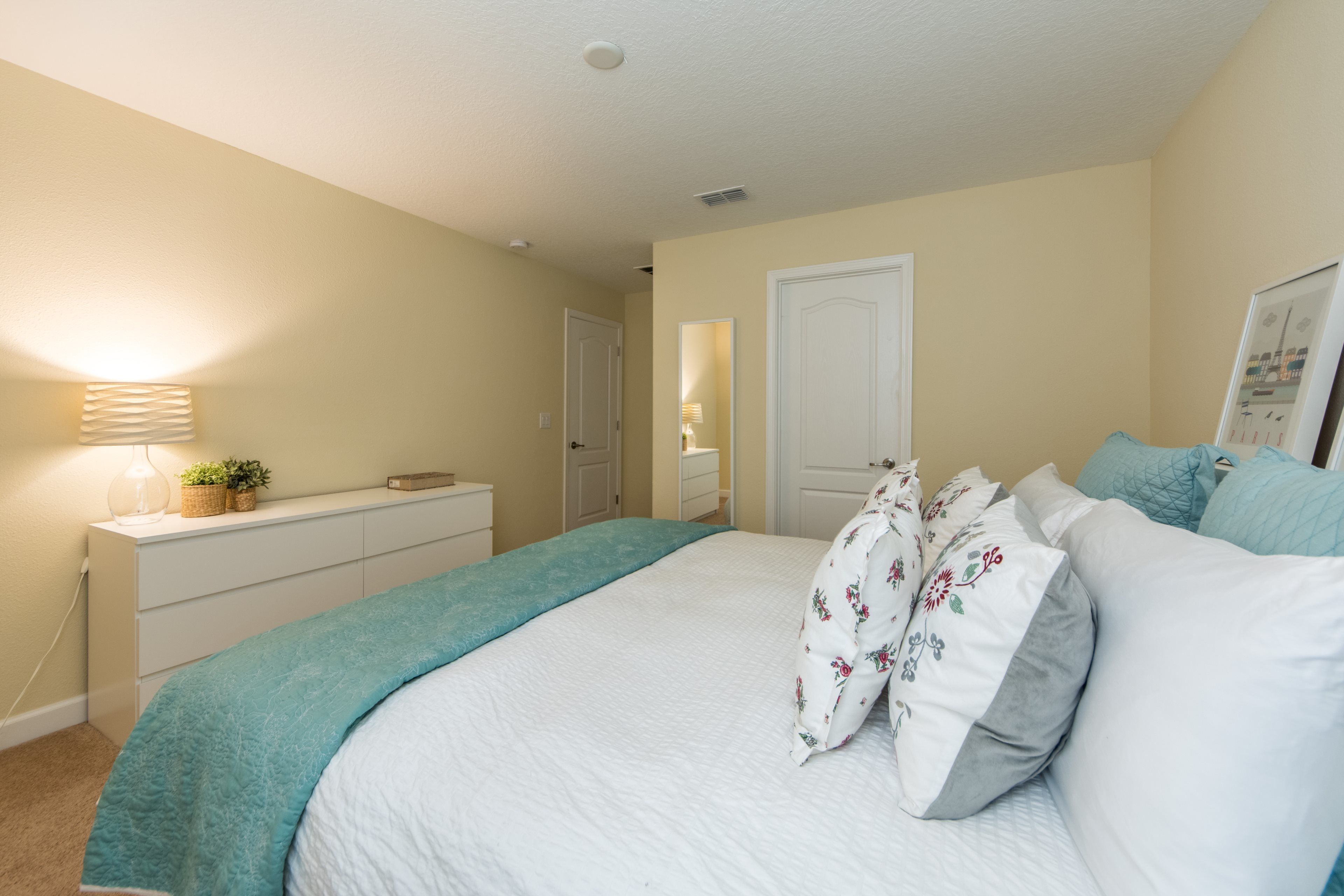 Une chambre à coucher avec un lit, une commode, une lampe et une porte.