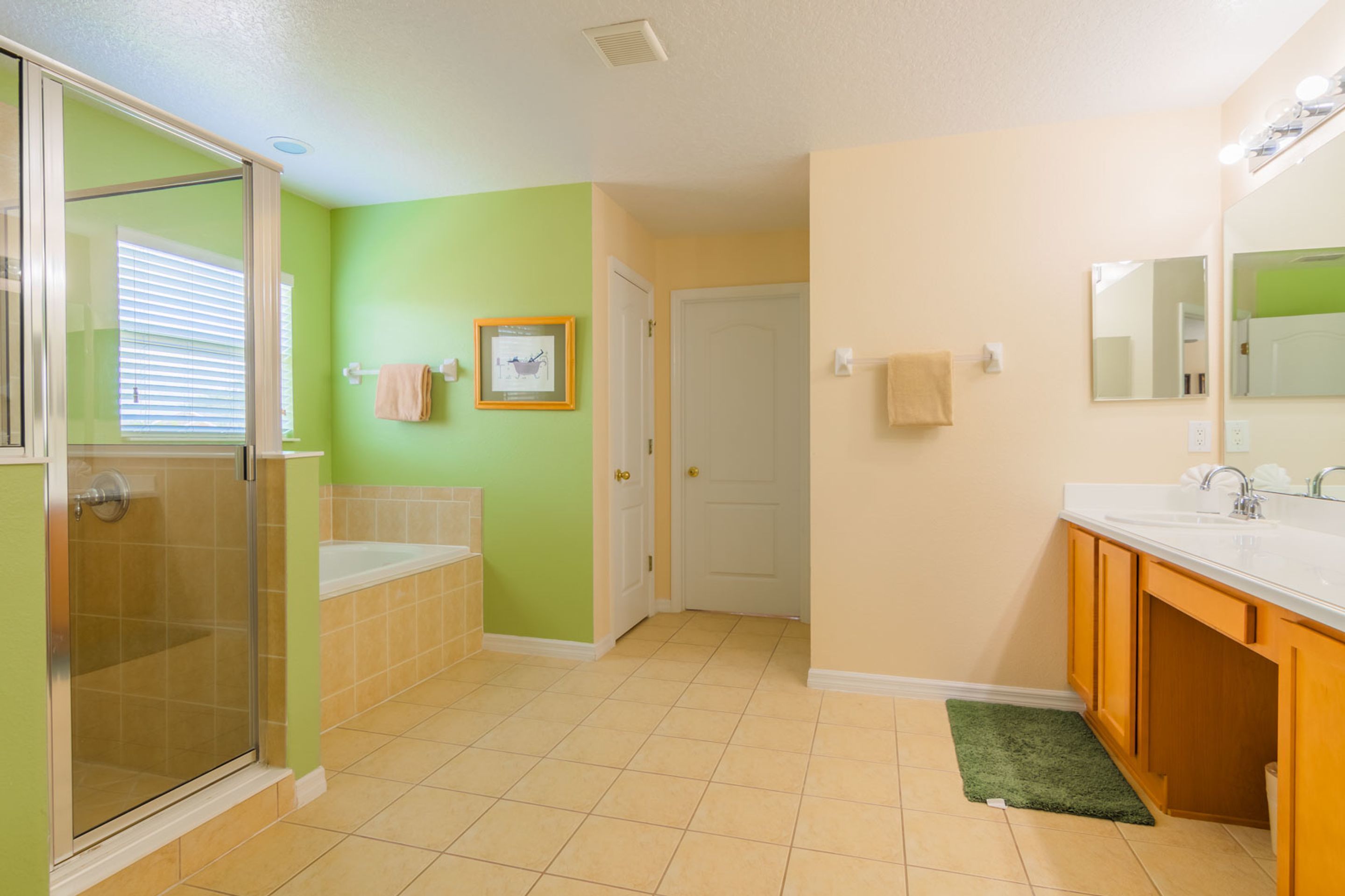 A bathroom with a glass shower enclosure, a sink with a mirror, and a door leading to another room.
