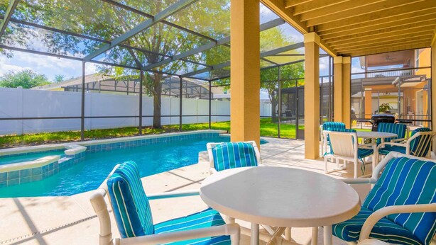 An outdoor pool area with lounge chairs and a table, surrounded by a pergola structure.
