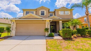 A two-story house with a garage, a covered driveway, and well-maintained landscaping including a palm tree and bushes.