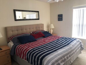 A bedroom with a bed, a nightstand, a lamp, a mirror, and a window. - Terra Verde Resort 4762 (Kissimmee)