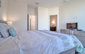 A bedroom with a large bed, a dresser, a television, and a bathroom visible through an open door.