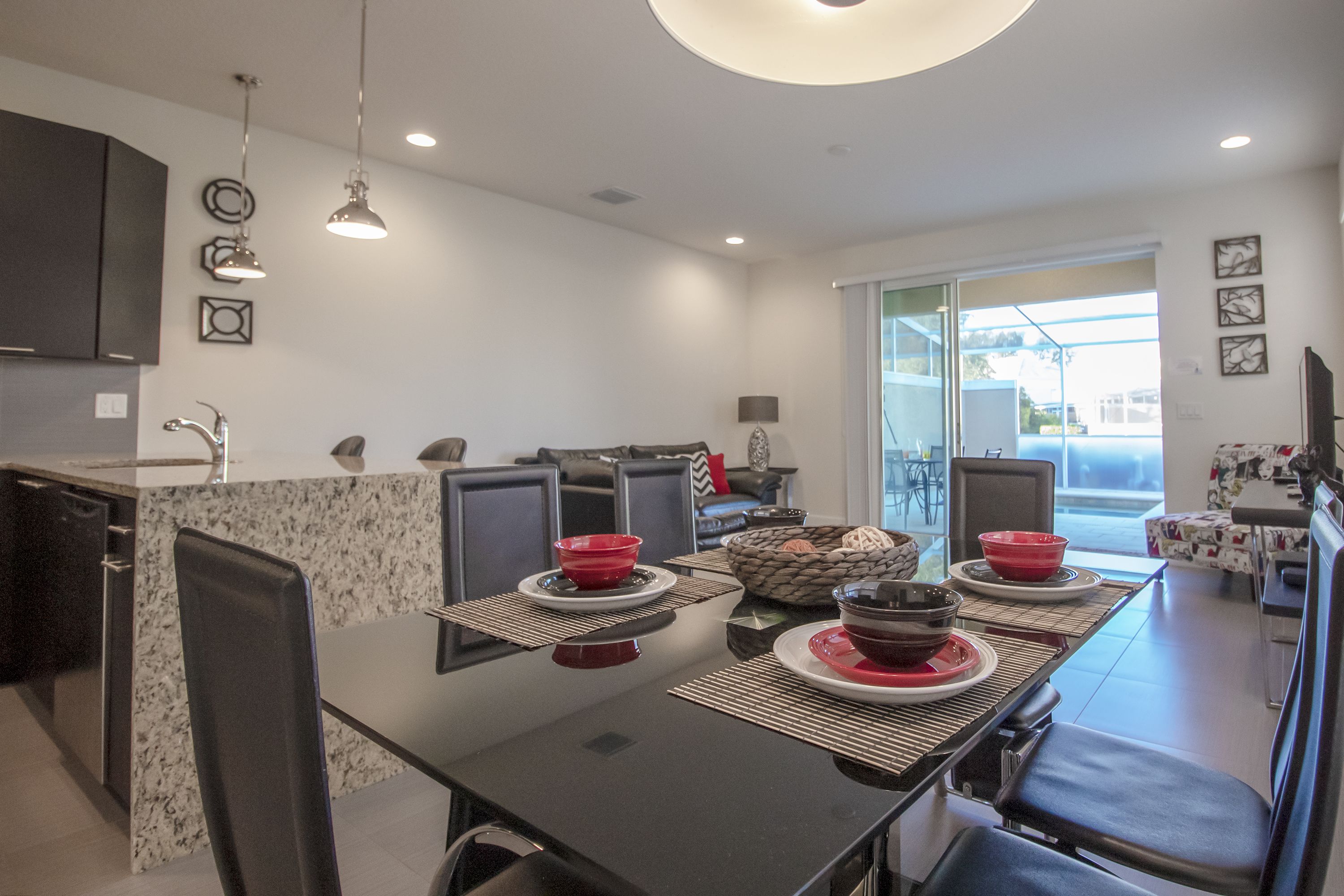 A modern kitchen with a dining area, featuring a black dining table with red bowls, black chairs, and a kitchen island with a sink and cabinets.