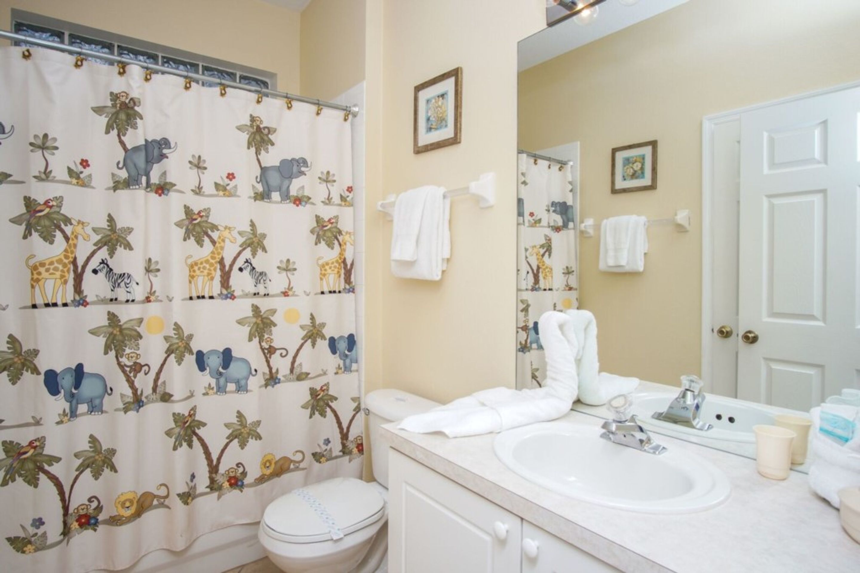 A bathroom with a shower curtain featuring animal prints, a toilet, a sink with a mirror, and towels hanging on the wall.