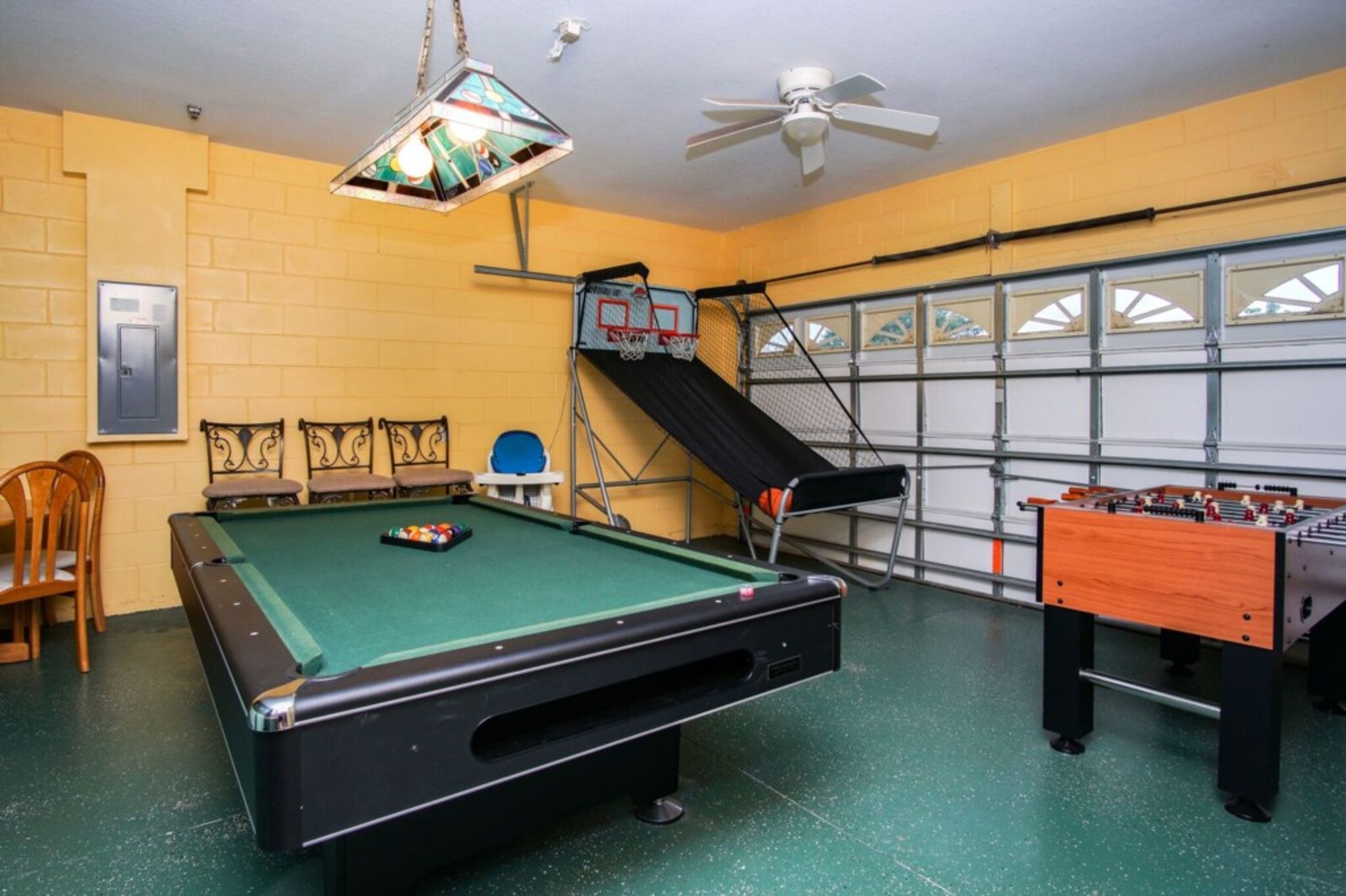 A pool table, a foosball table, and a chair in a room with yellow walls and a garage door.