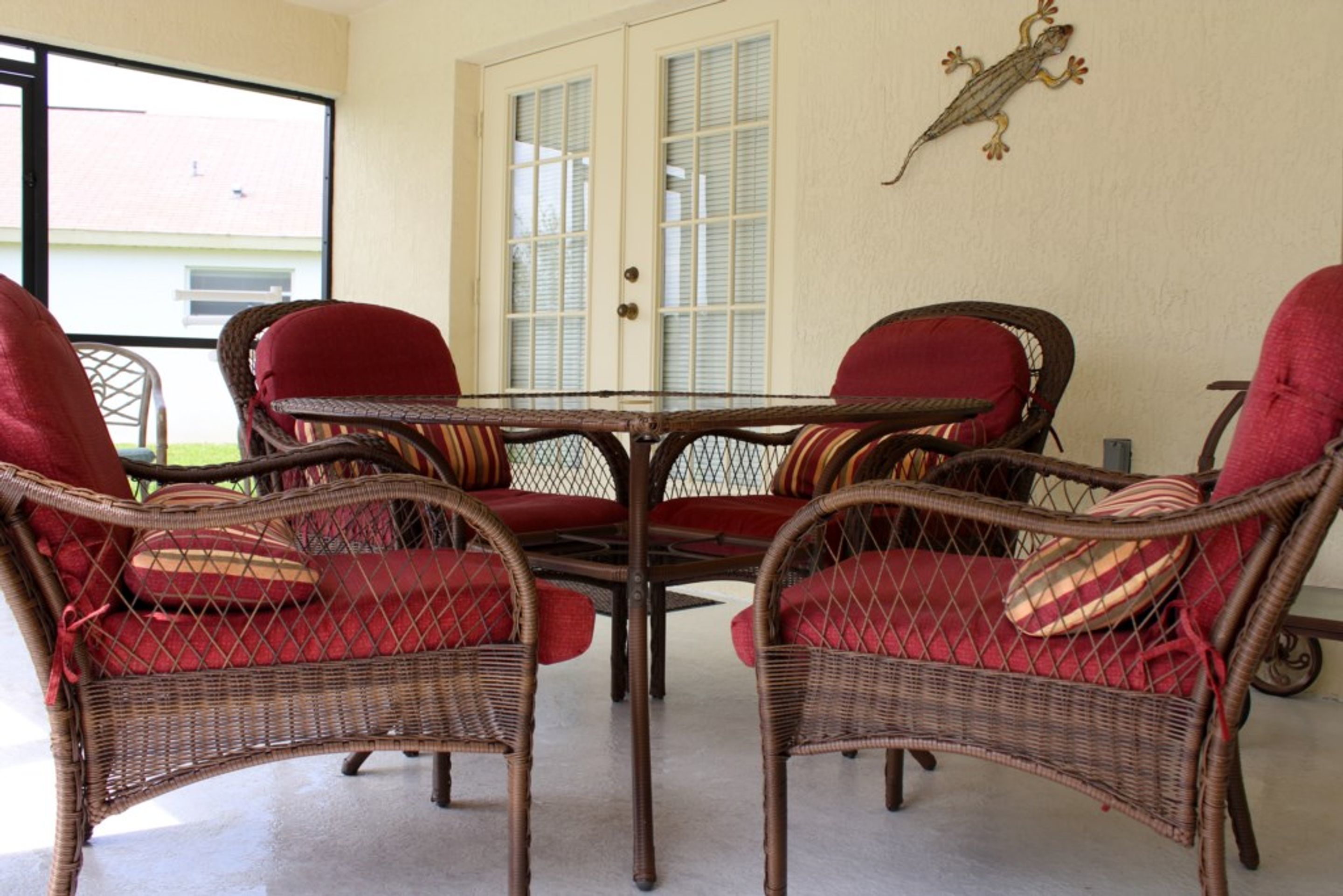 A patio with wicker chairs and a table, a door with glass panels, and a wall-mounted lizard decoration.