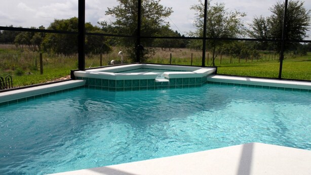 A swimming pool with a hot tub area, surrounded by a fence and trees. - Orange Tree 3434 (Clermont)