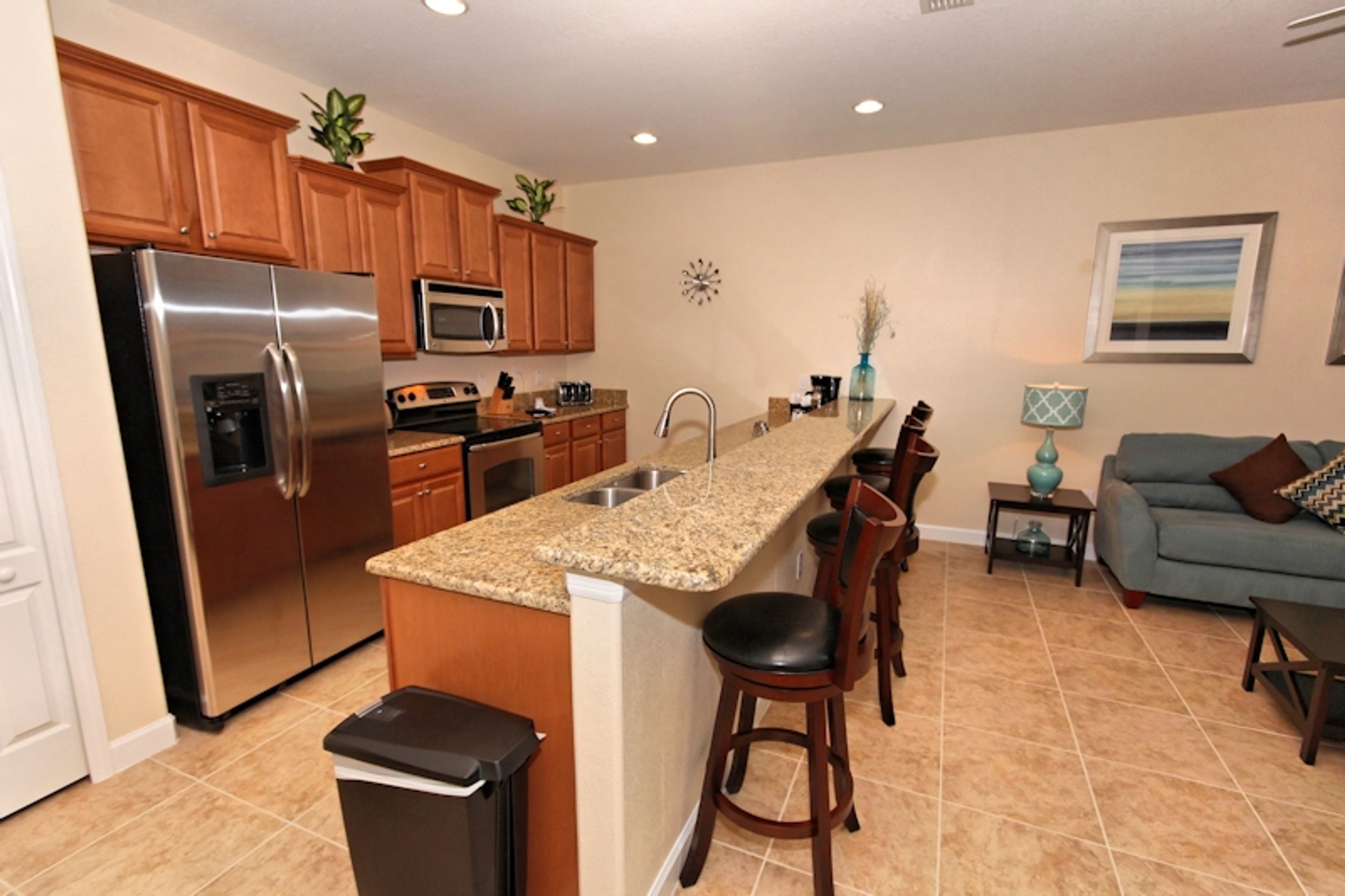A modern kitchen with a stainless steel refrigerator, granite countertop, wooden cabinets, and a built-in microwave.