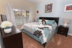 A bedroom with a bed, a nightstand, a dresser, a window with curtains, and wall art. - Paradise Palms 8899 (Kissimmee)