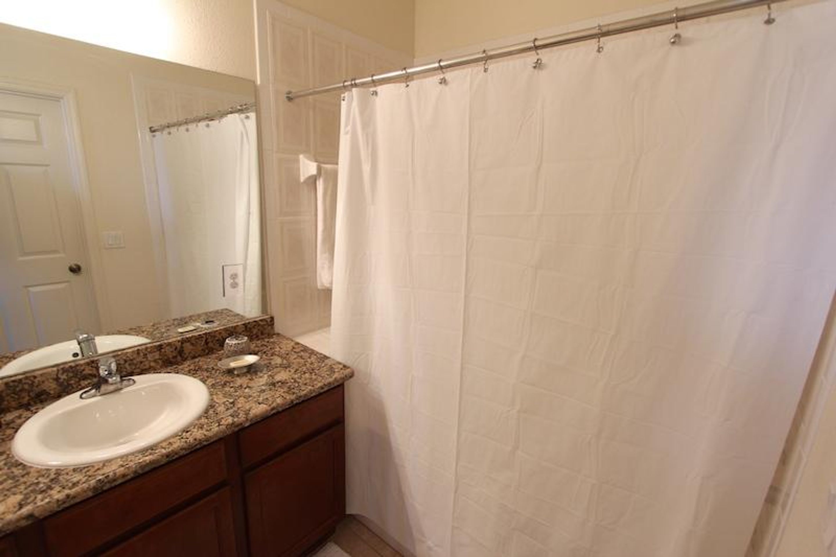 A bathroom with a double sink, a mirror, a shower curtain, and a towel rack.