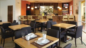Un restaurant doté de nombreuses tables et chaises, un bar avec des étagères remplies de bouteilles et une grande fenêtre offrant une vue panoramique.
