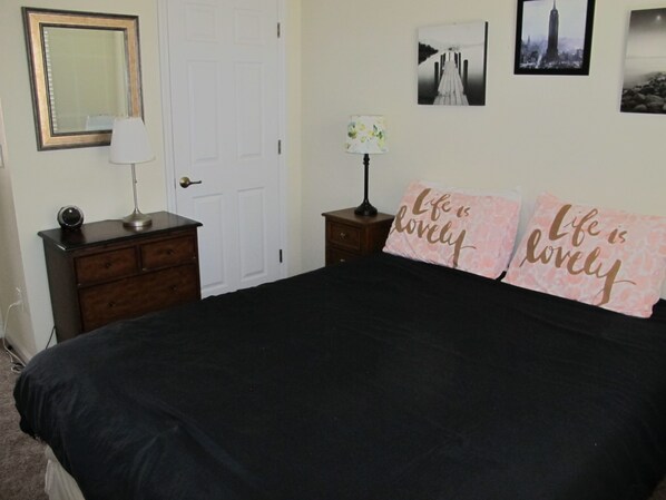 A bedroom with a bed, a dresser, a lamp, a mirror, and two pillows with the text "Life is lovely".