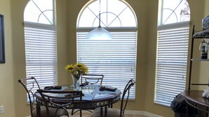 A dining area with a round table, four chairs, a vase with flowers, and large windows with blinds. - Crystal Cove 4768 (Kissimmee)