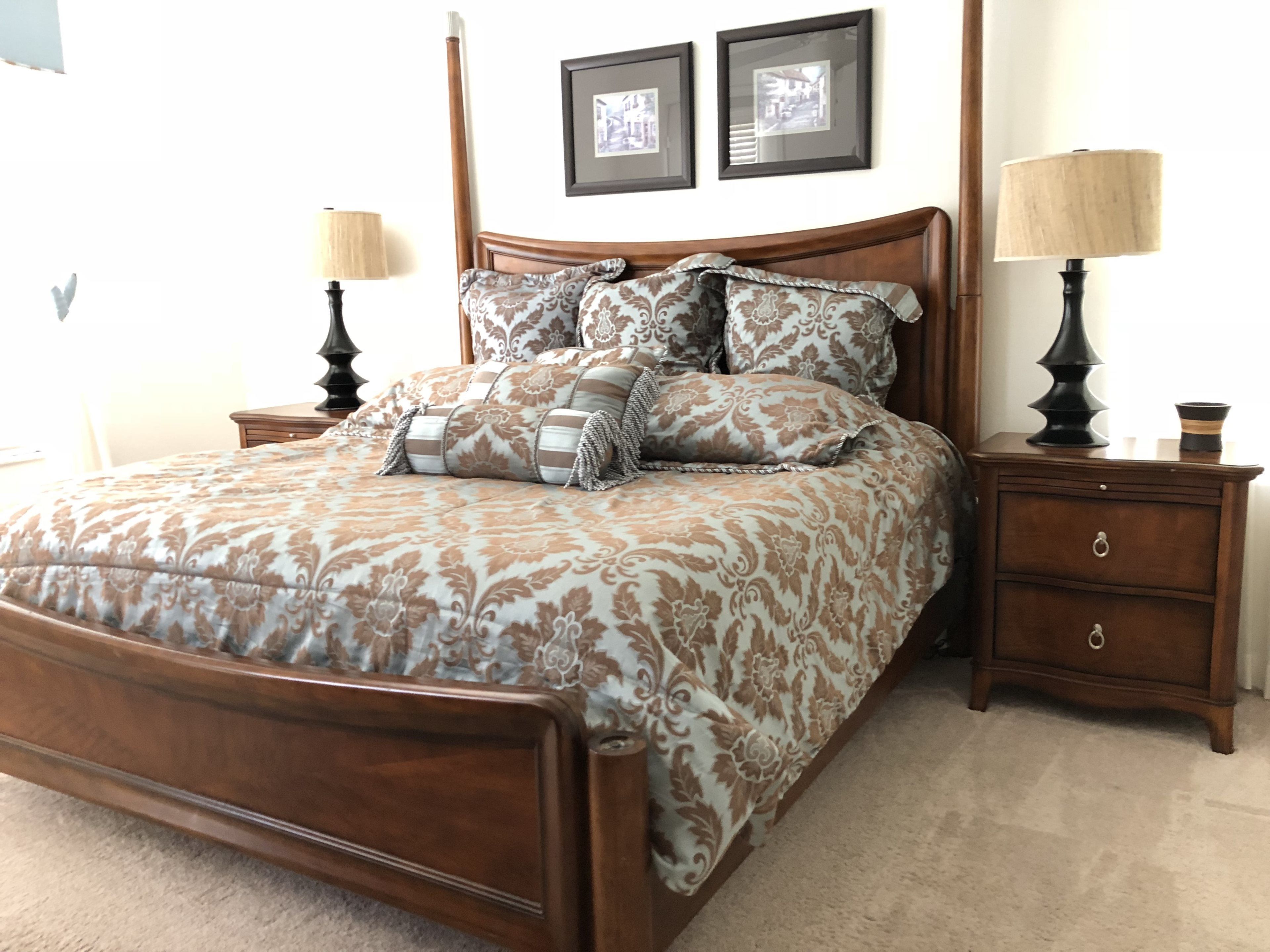 A bedroom with a wooden bed, patterned bedding, two bedside tables with lamps, and framed pictures on the wall.