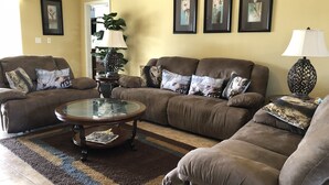 A living room with two brown sofas, a glass coffee table, and a patterned rug. There are three framed artworks on the wall and a lamp on a side table. - Crystal Cove 4768 (Kissimmee)