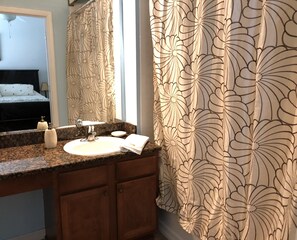 Ein Badezimmer mit einer Granitplatte, einem Waschbecken, einem Spiegel und einem Duschvorhang mit Blumenmuster.