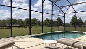 A pool area with lounge chairs and a view of a grassy field through a glass enclosure. - Crystal Cove 4768 (Kissimmee)