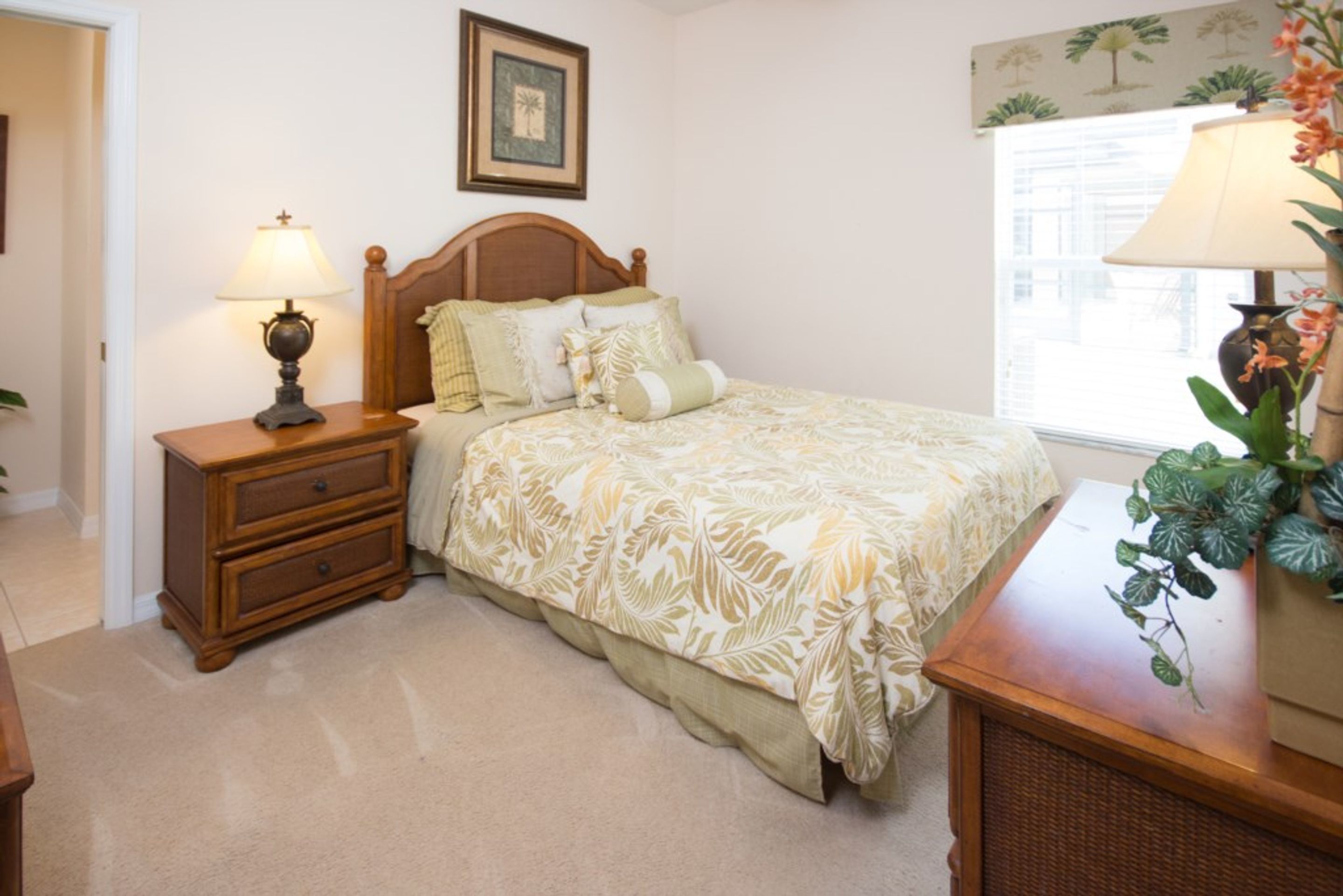 Une chambre à coucher comprenant un lit, une table de chevet, une commode et une fenêtre avec des rideaux.